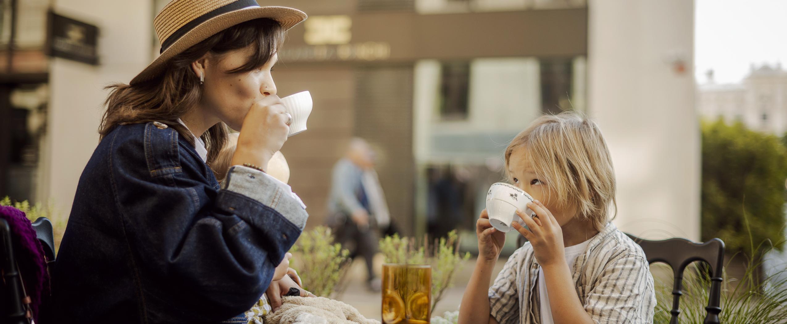 Молодая женщина с двумя маленькими детьми отдыхает в кафе, на фоне виден жилой квартал CENTRUS на улице Dzirnavu.